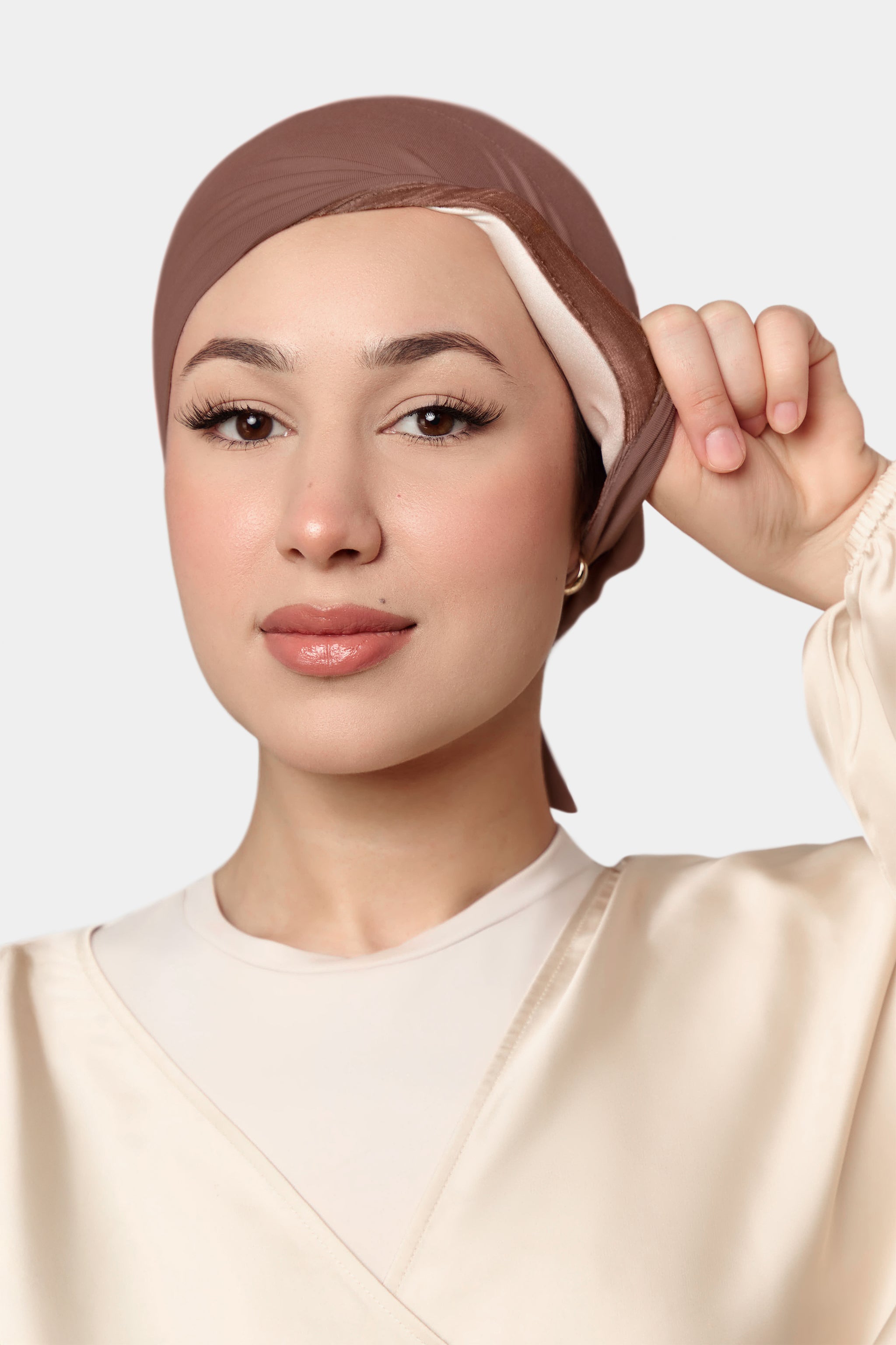 Woman wearing a brown underscarf against a light background