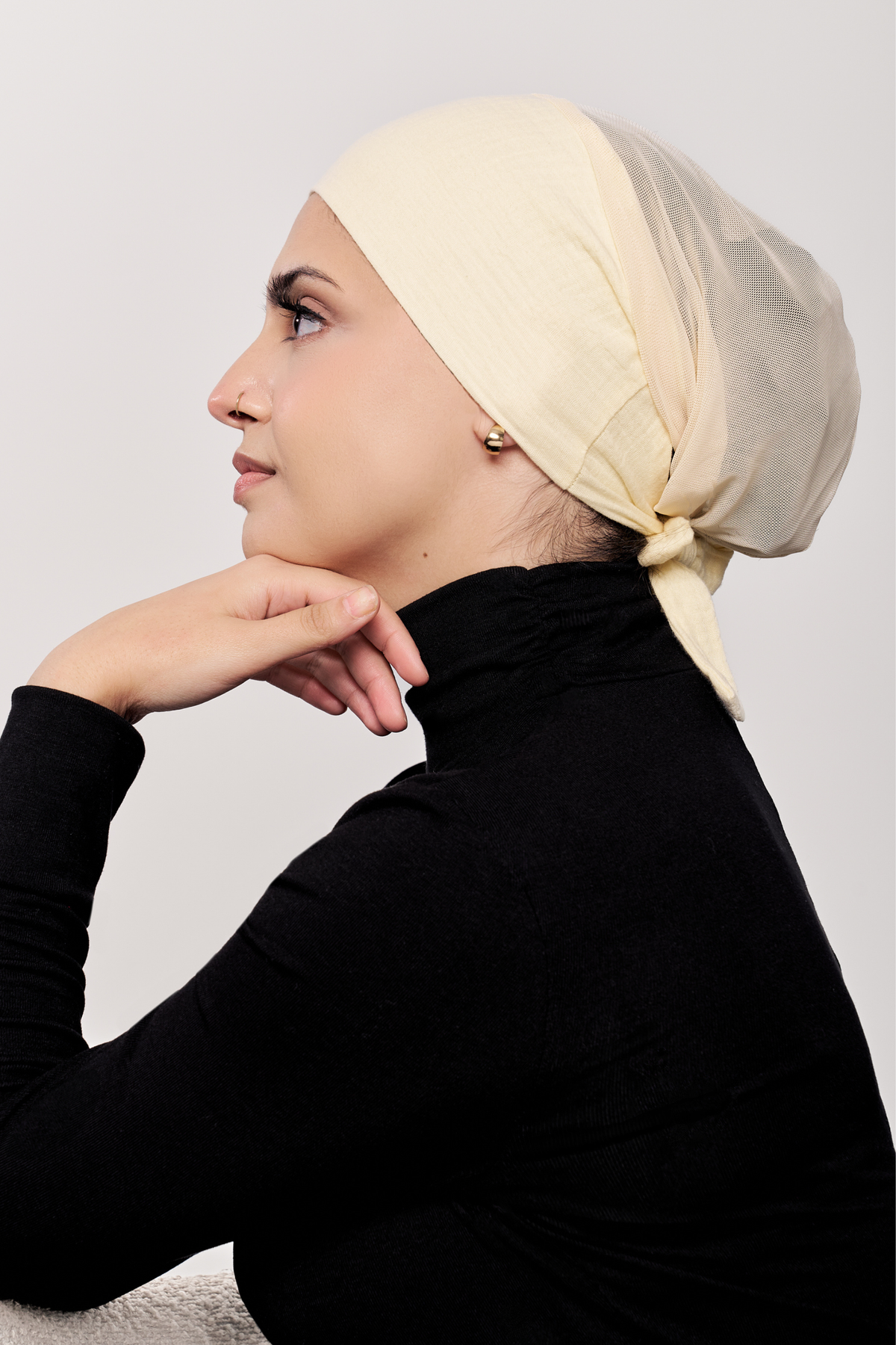 A woman wearing a buttercream underscarf and a black mock-neck long-sleeve top, posed against a light gray background.
